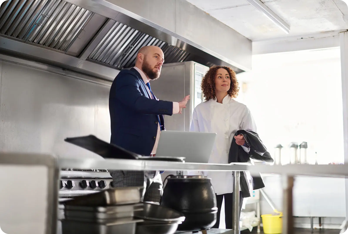 Two people discussing in a professional kitchen.